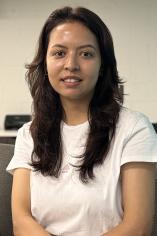 Mahdia Ahmadi half body shot. She is in a white short sleeve shirt. Background has computers.