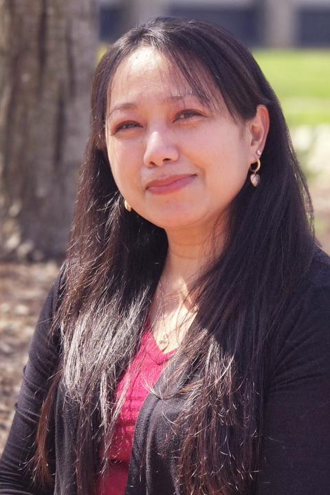Image of female with long dark hair, red inside shirt, black cardigan, outdoor nature setting.