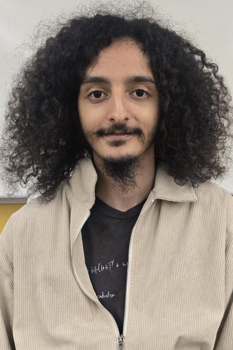 image of a male student wearing brownish jacket and black inside t-shrit, with generous thick curly hair