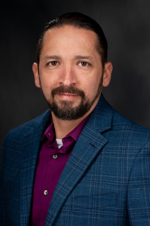 Dark-haired man in wine-colored shirt and checked-blue suit coat