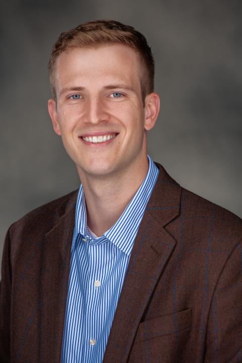 Asst. Professor Loren Hahn dressed professionally in a blue and white button up shirt under a dark blazer. 