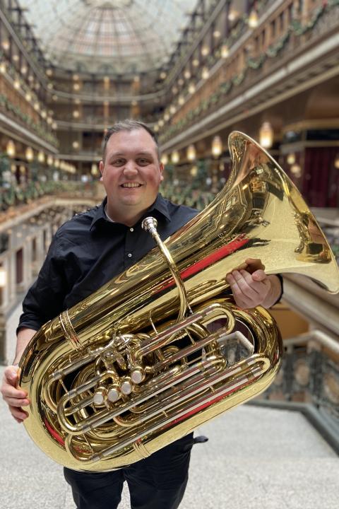 Man holding a tuba standing inside a building