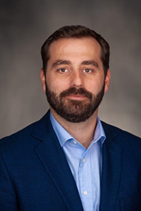 A man with dark hair and short beard in a blue suit and light blue shirt