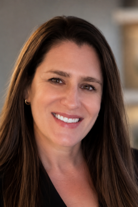 Portrait of a smiling woman with long brown hair wearing a black sleeveless top.