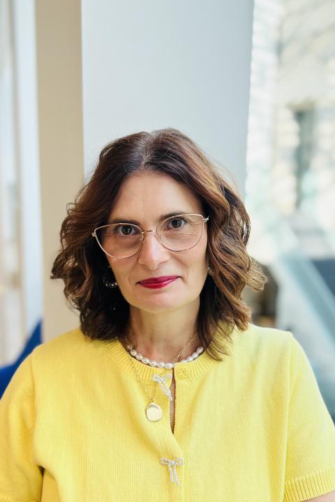 Headshot of woman with brown hair, yellow blouse and glasses