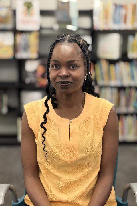 Esther Popoola in a yellow shirt with a background of books on a shelf
