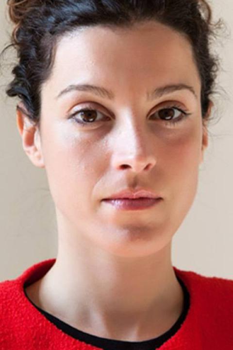 Close up portrait of woman with neutral expression wearing a red shirt, her dark brown hair in an updo