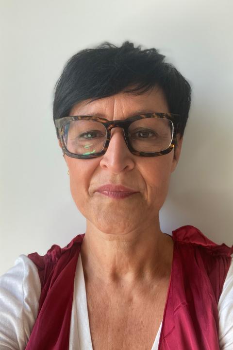 Headshot of Silvia, her hair dark and close-cropped to her ears. She wears large, square dark brown glasses