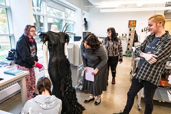 Group of students study a black garment in a fashion studio. 