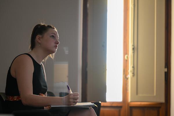 Photo of a young woman in a dress sitting at a desk taking notes