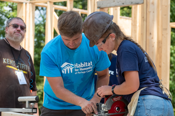 A student uses a circular saw at a Habitat for Humanity construction site as part of a volunteer event.