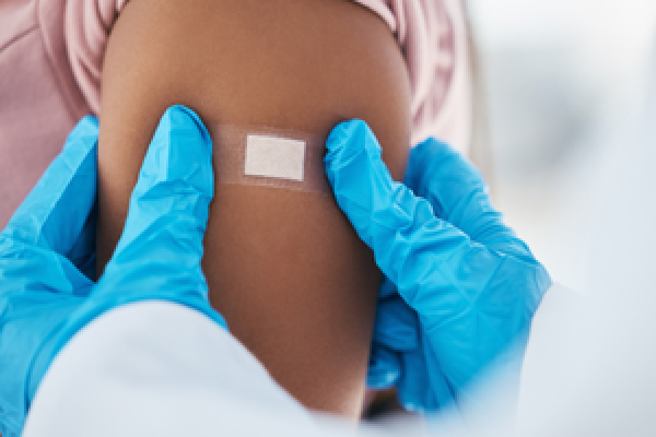 A pair of gloved doctor hands pressing a band-aid onto a patient's arm, showing they just got their flu shot.