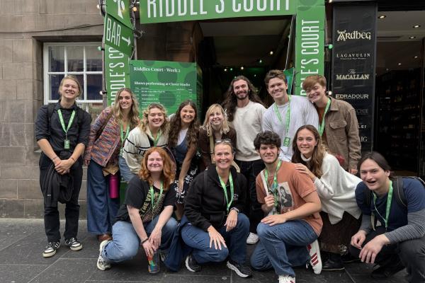 A group shot of participants posing in front of a green sign, many wearing green necklaces