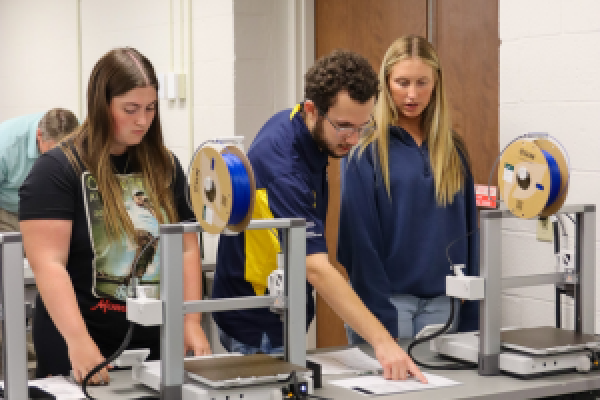 A group of students gathered around equipment in the IRC Resource Lab, learning how to use it.