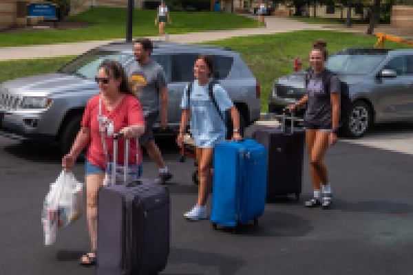 Incoming freshmen rolling suitcases towards a dorm