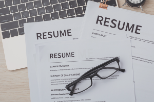 A stack of resumes sitting on a laptop keyboard.