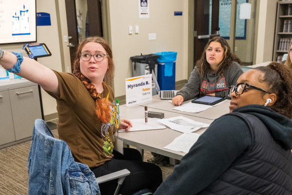 Three students sit at a table in the Academic Success Center with a tutor.