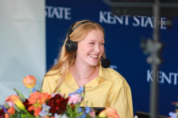 Student Sydney Brown poses with flowers while wearing a broadcast headset