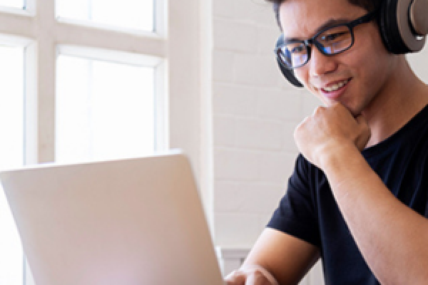 A person sitting at a laptop with headphones on, taking an online course.