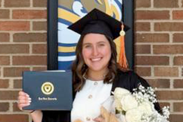 Olivia Voyzey holding her diploma win the cap and gown.