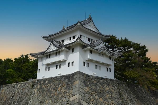 A white building with a stone wall and sunset in the background.