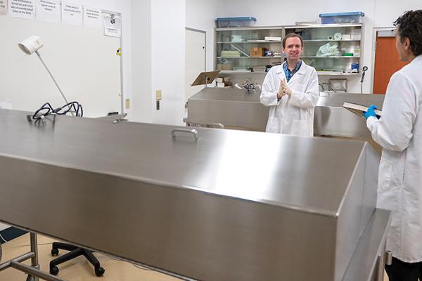 Two men in lab coats have a discussion in the Ashtabula Campus cadaver lab