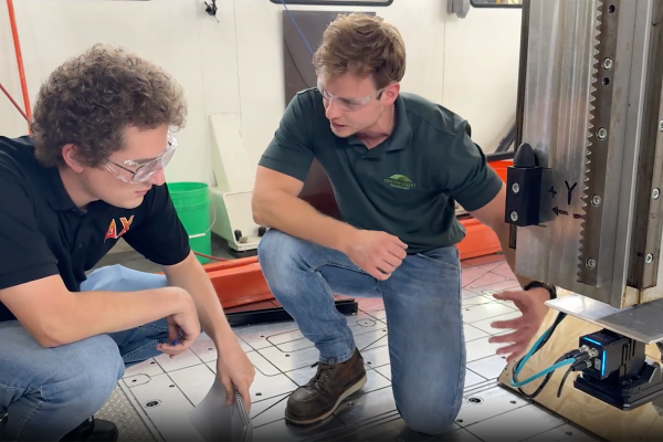 A student intern with curly hair kneels next to a large printing machine