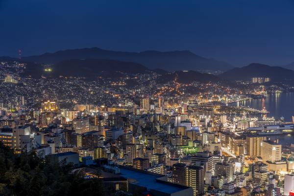 Cityscape of Nagasaki at night, several buildings and night lights with mountains in the horizon, Japan.