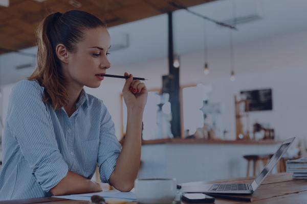 A woman works on the computer intently, while chewing on a pencil.