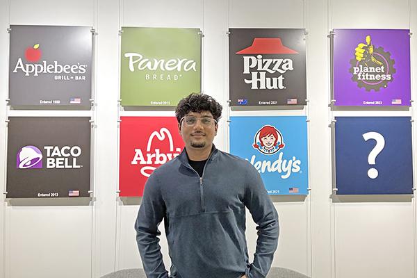 A young man wearing a blue sweater standing in front of several restaurant logos.