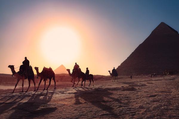 People riding camels by the pyramids during sunset, in Cairo, Egypt.