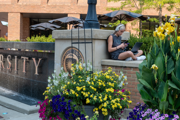 A student studies by a Kent State sign and colorful flowers.