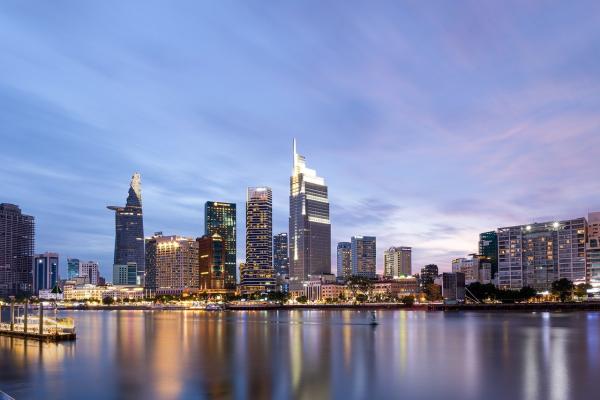 Cityscape at dawn, buildings by the river, boats, night lights.