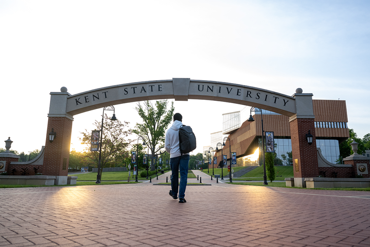 A student walks under the Kent State arch at sunrise.