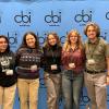 Five Kent State student media participants stand side by side, smiling in front of a blue College Broadcasters Inc. (CBI) step-and-repeat backdrop at a national conference.