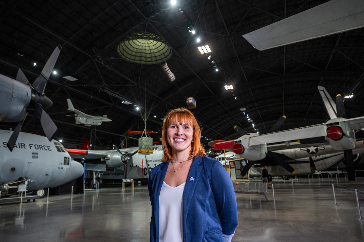 Victoria Bylsma, M.P.H., standing in an Air Force museum hangar with aircraft behind her.